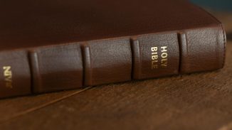 A close-up of a brown leather-bound Holy Bible resting on a wooden surface.